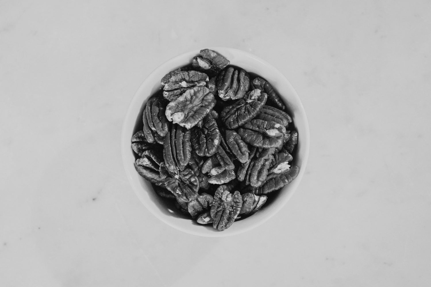 Pecans in a circular white container on a light gray background
