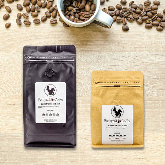 Two coffee packages from Bushytail Coffee on a wooden surface with coffee beans and a cup.