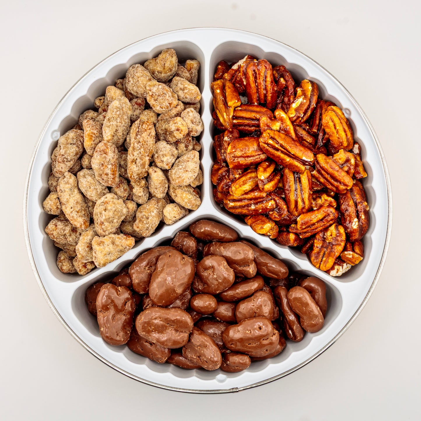 Praline, Honey-Glazed, and Milk Chocolate Pecans in a gift tin on a white background