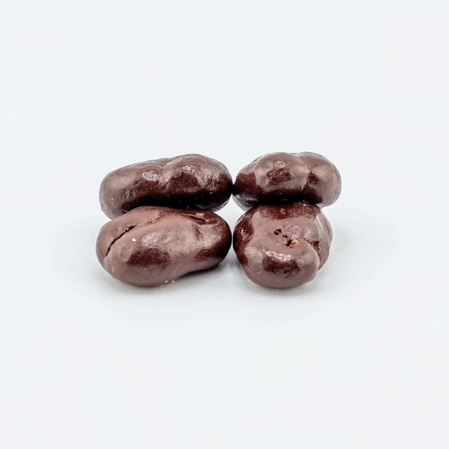 Four dark chocolate-covered pecans on a white background