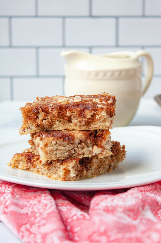 Stacked cinnamon pecan sheet pan pancakes with syrup container in background. 
