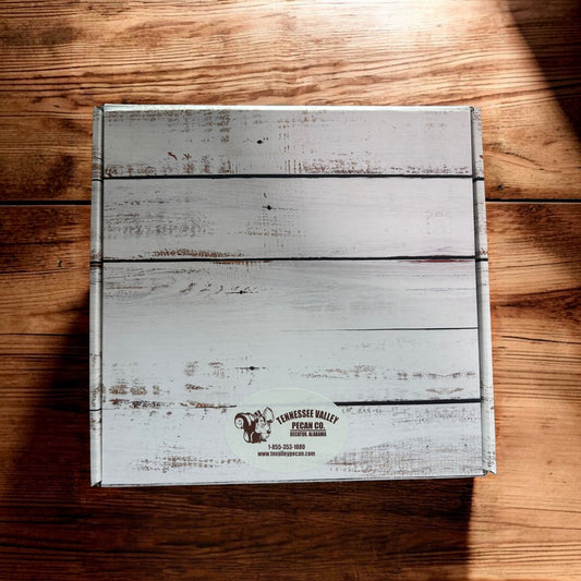 A square gift box with a distressed white wood plank design sits on a brown wooden tabletop. A small oval label at the bottom reads Tennessee Valley Creamery.