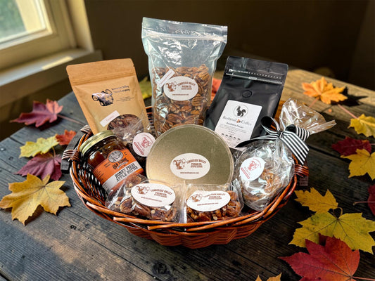 A fall-themed gourmet gift basket filled with various packaged snacks and treats, including pecans, coffee, and pecan butter, arranged on a rustic wooden table with scattered autumn leaves.