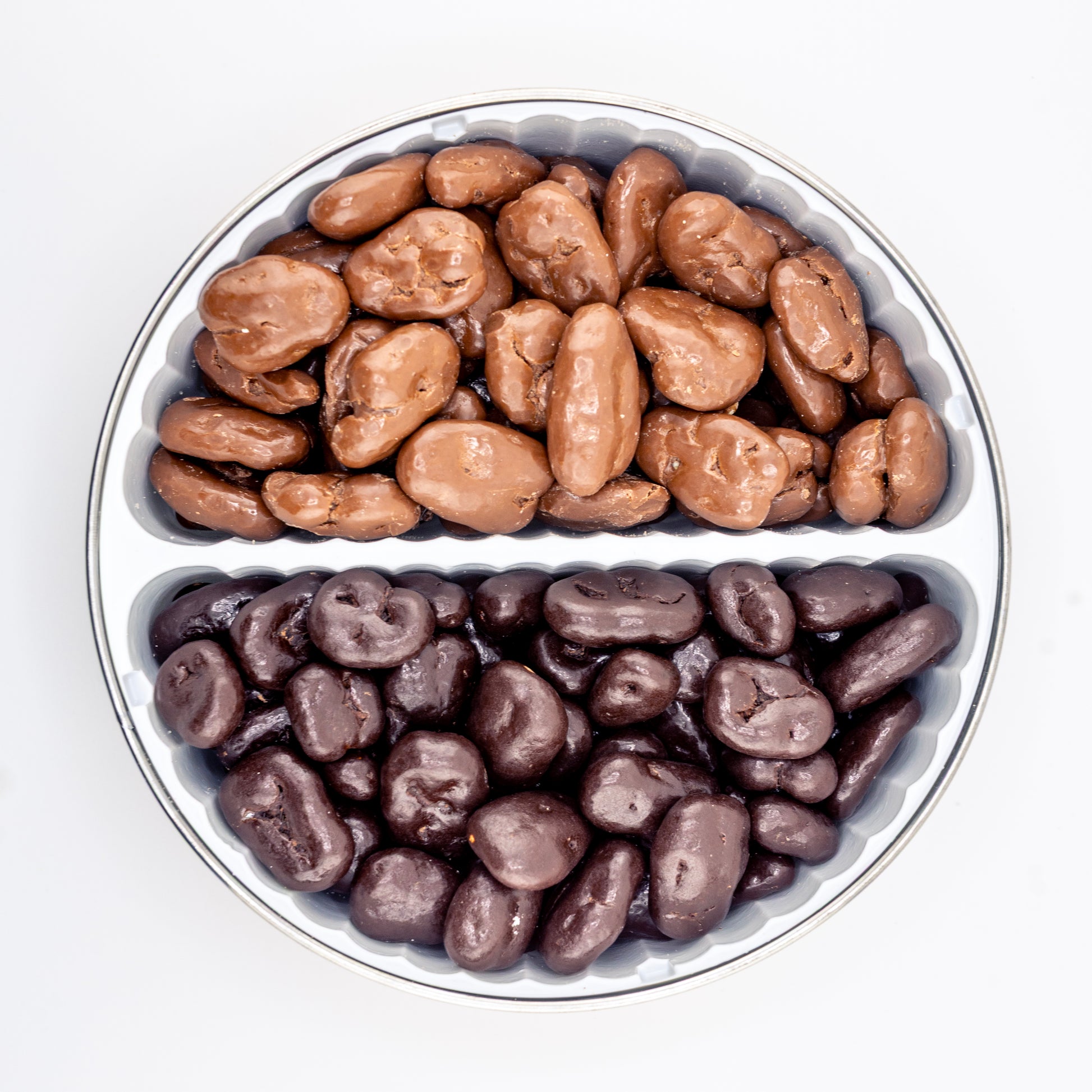 Dark and milk chocolate pecans in a divided tin on white background.
