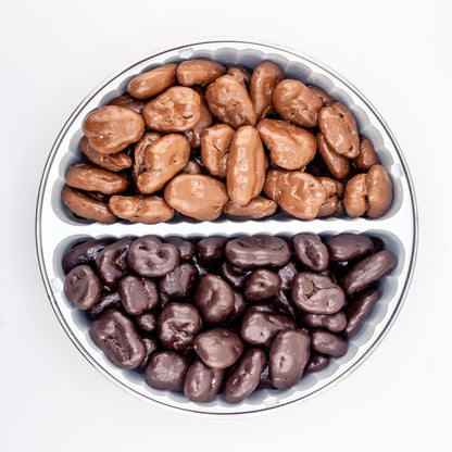 Dark and milk chocolate pecans in a divided tin on white background.