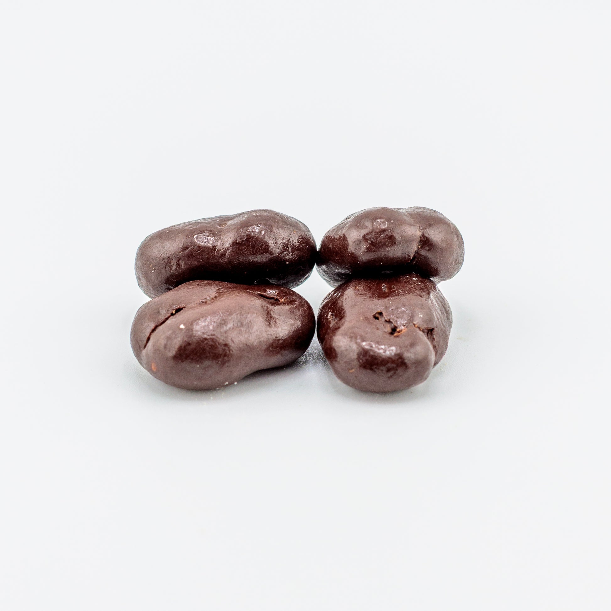 Four dark chocolate-covered pecans on a white background