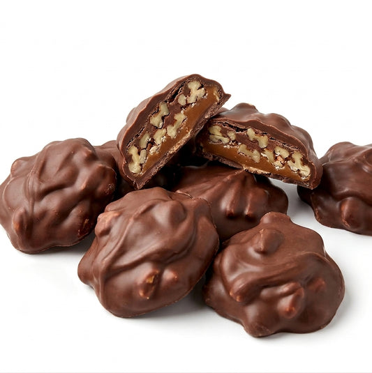 A pile of milk chocolate candy-coated nuts, with two pieces broken open to reveal a pecan-filled caramel center, set against a plain white background.